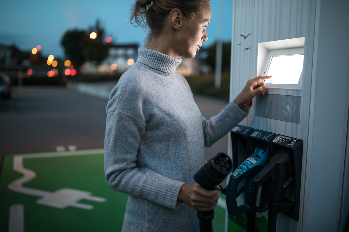 Young woman charging an electric vehicle. Car sharing concept.